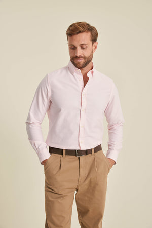 Man wearing a light pink dress shirt and beige pants against a plain background