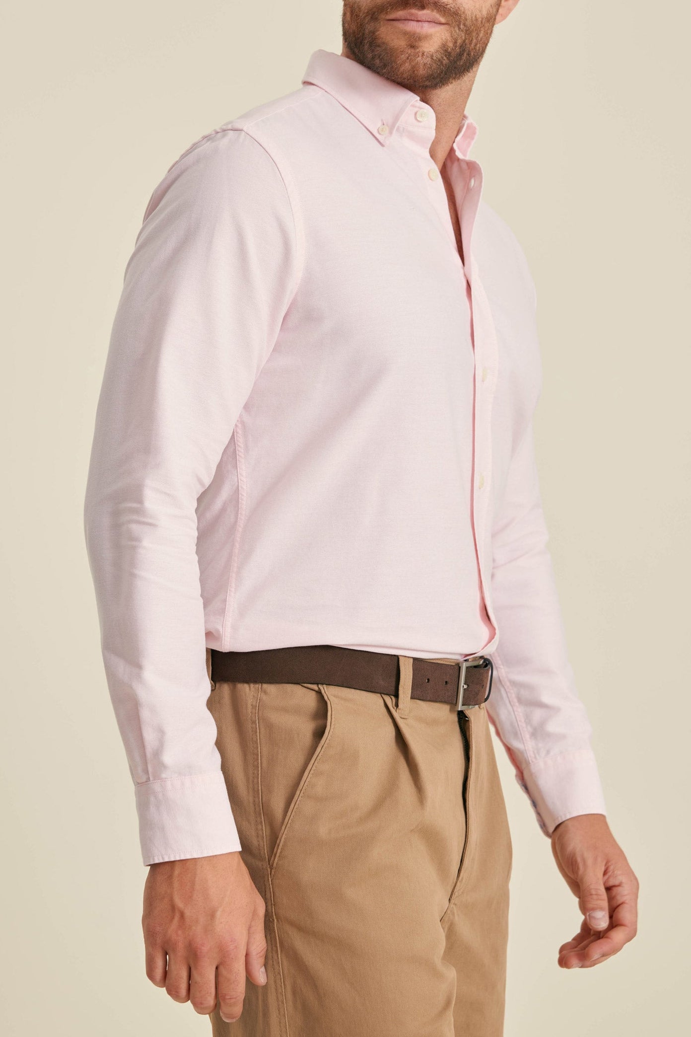 Man wearing a light pink dress shirt and beige pants on a beige background