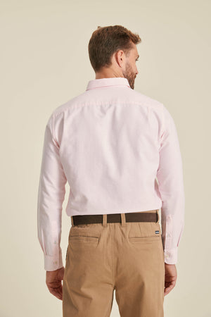 Man wearing a light pink dress shirt and beige pants on a beige background