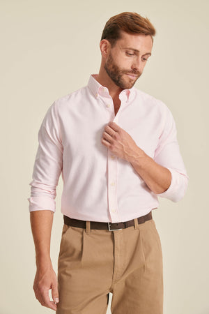 Man wearing a light pink shirt and beige pants against a plain background