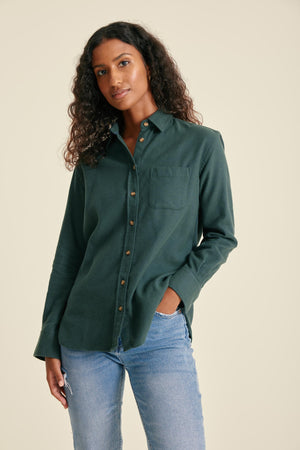 Woman wearing a green shirt and blue jeans against a beige background