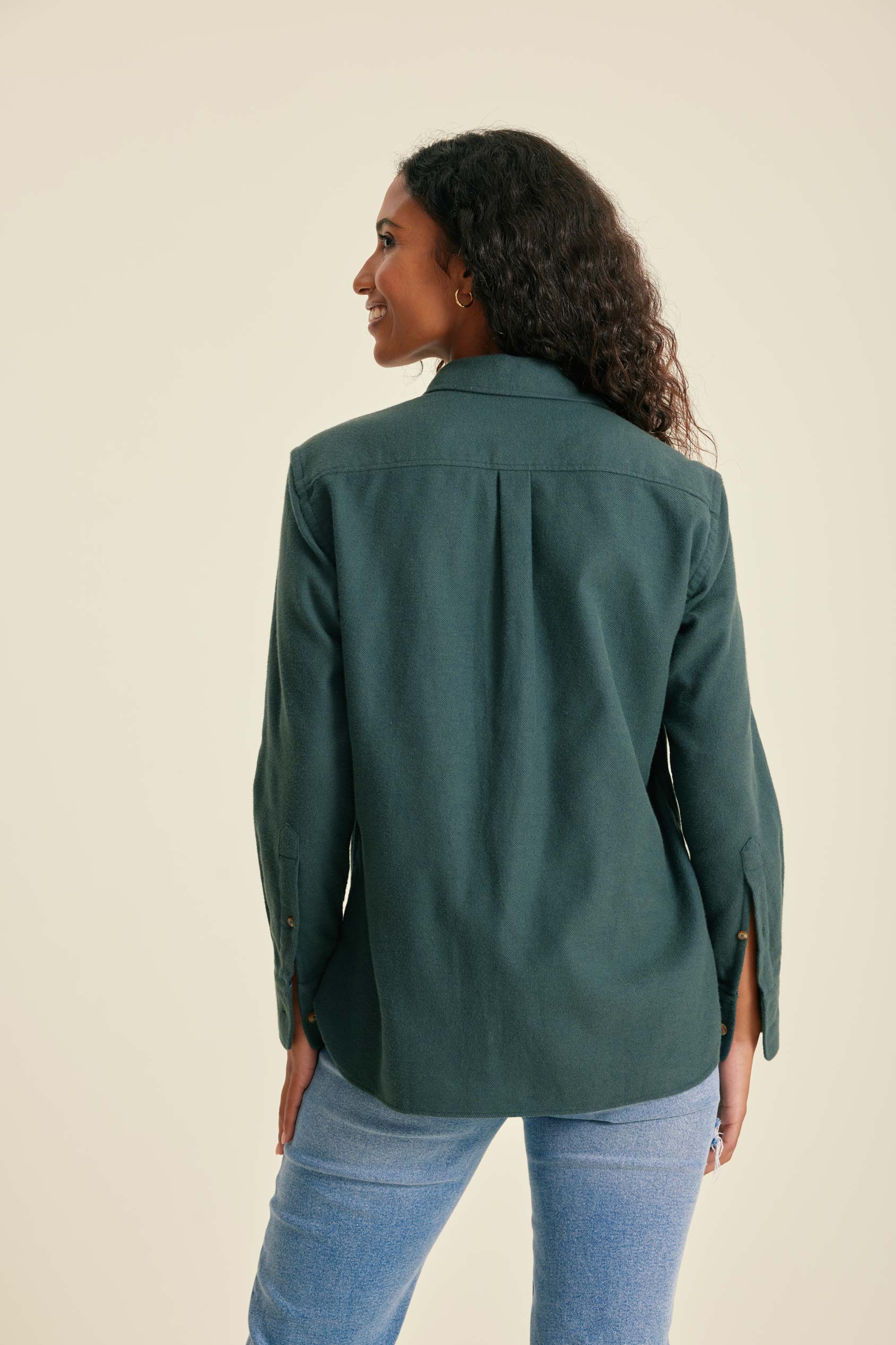 Person wearing a green jacket and blue jeans on a beige background
