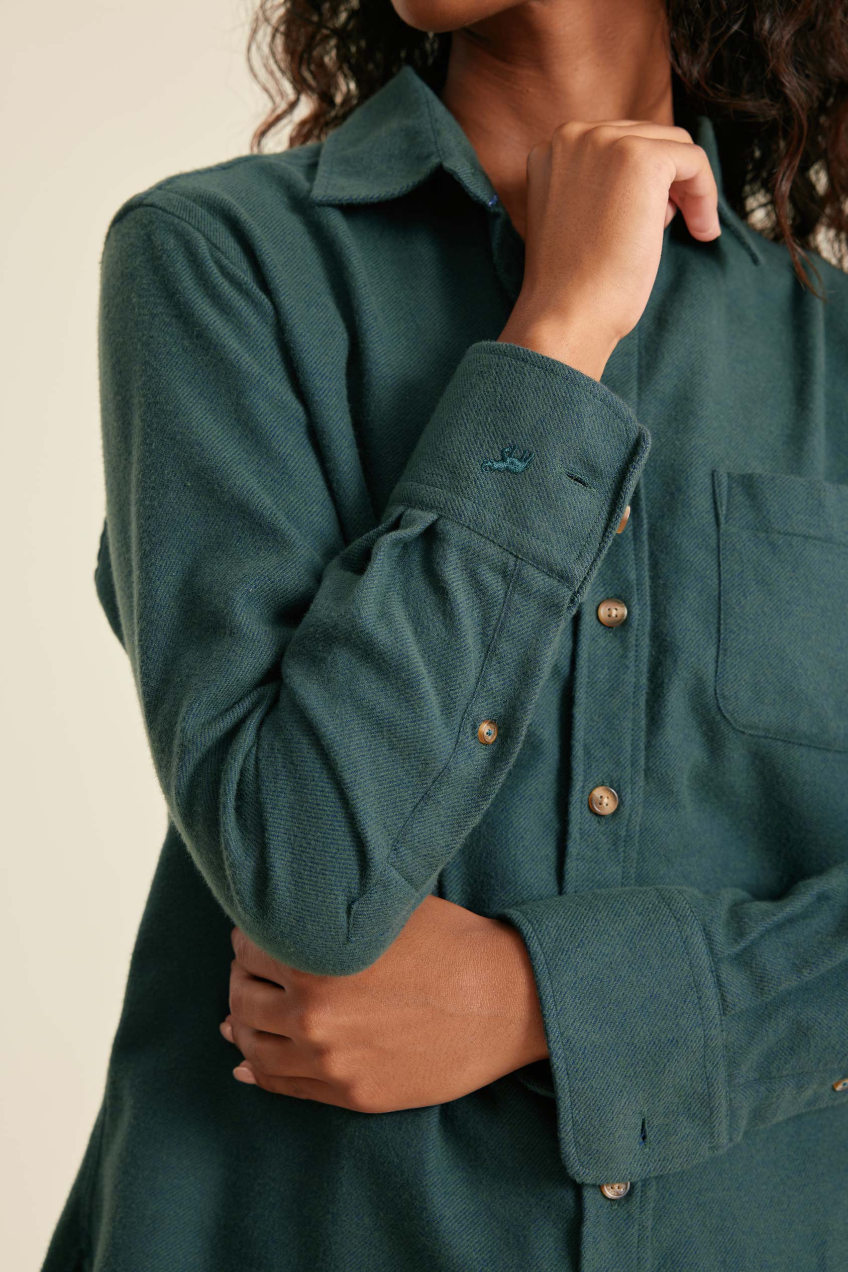 Teal shirt with buttons worn by a person on a beige background