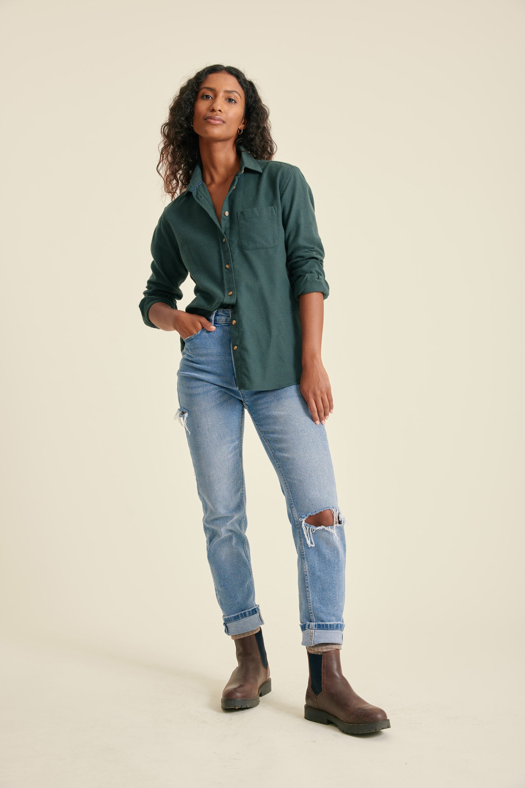Woman wearing a green shirt, blue jeans, and brown boots on a beige background