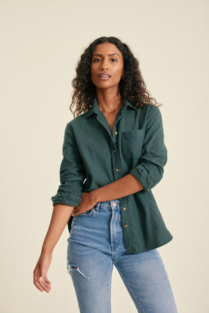 Woman wearing a green shirt and blue jeans against a beige background