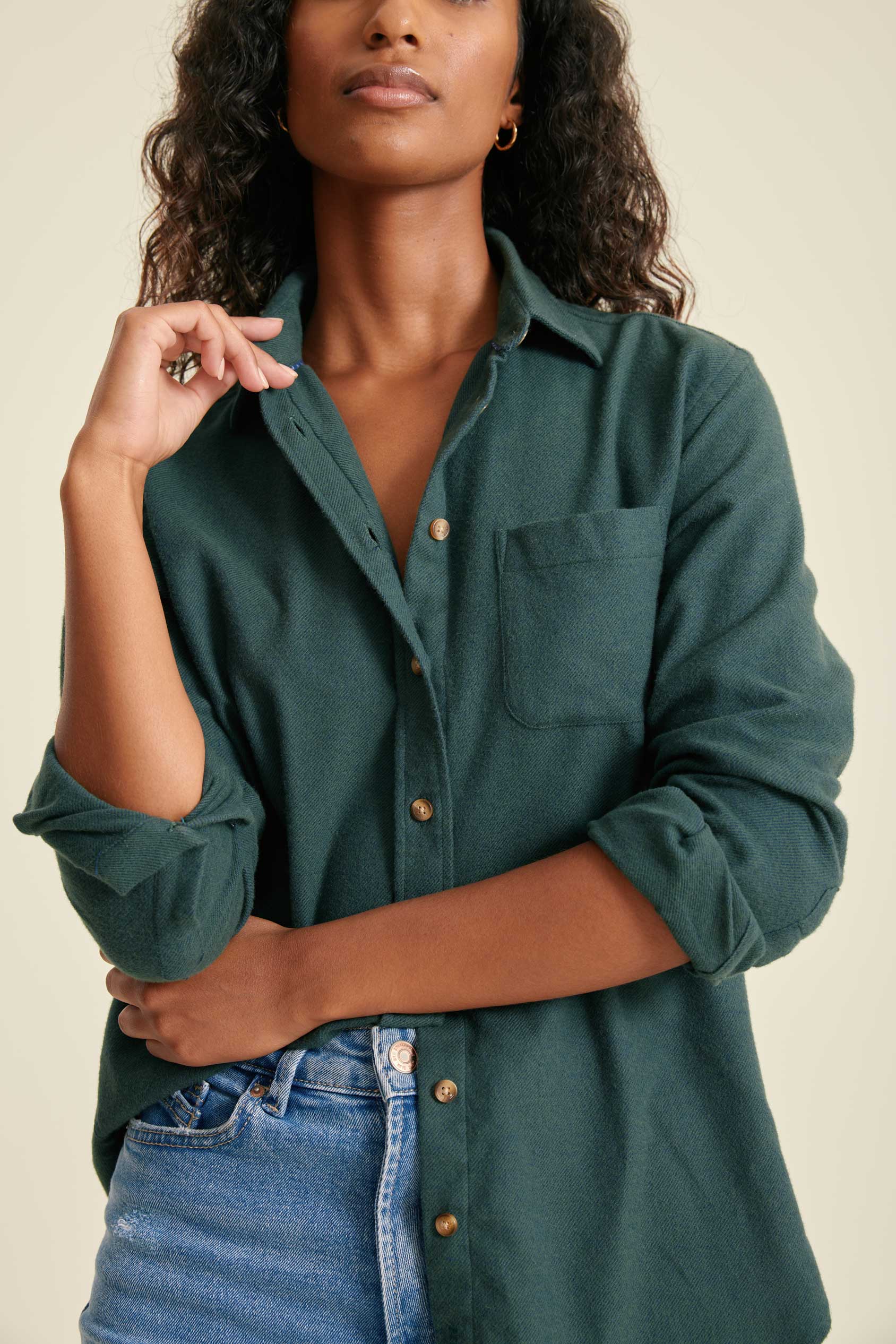 Woman wearing a green button-up shirt and blue jeans against a beige background