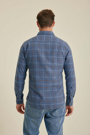 Man wearing a blue plaid shirt and jeans on a beige background