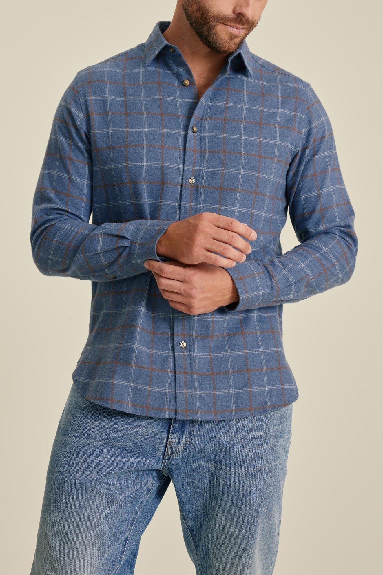 Man wearing a blue checkered shirt and jeans on a beige background