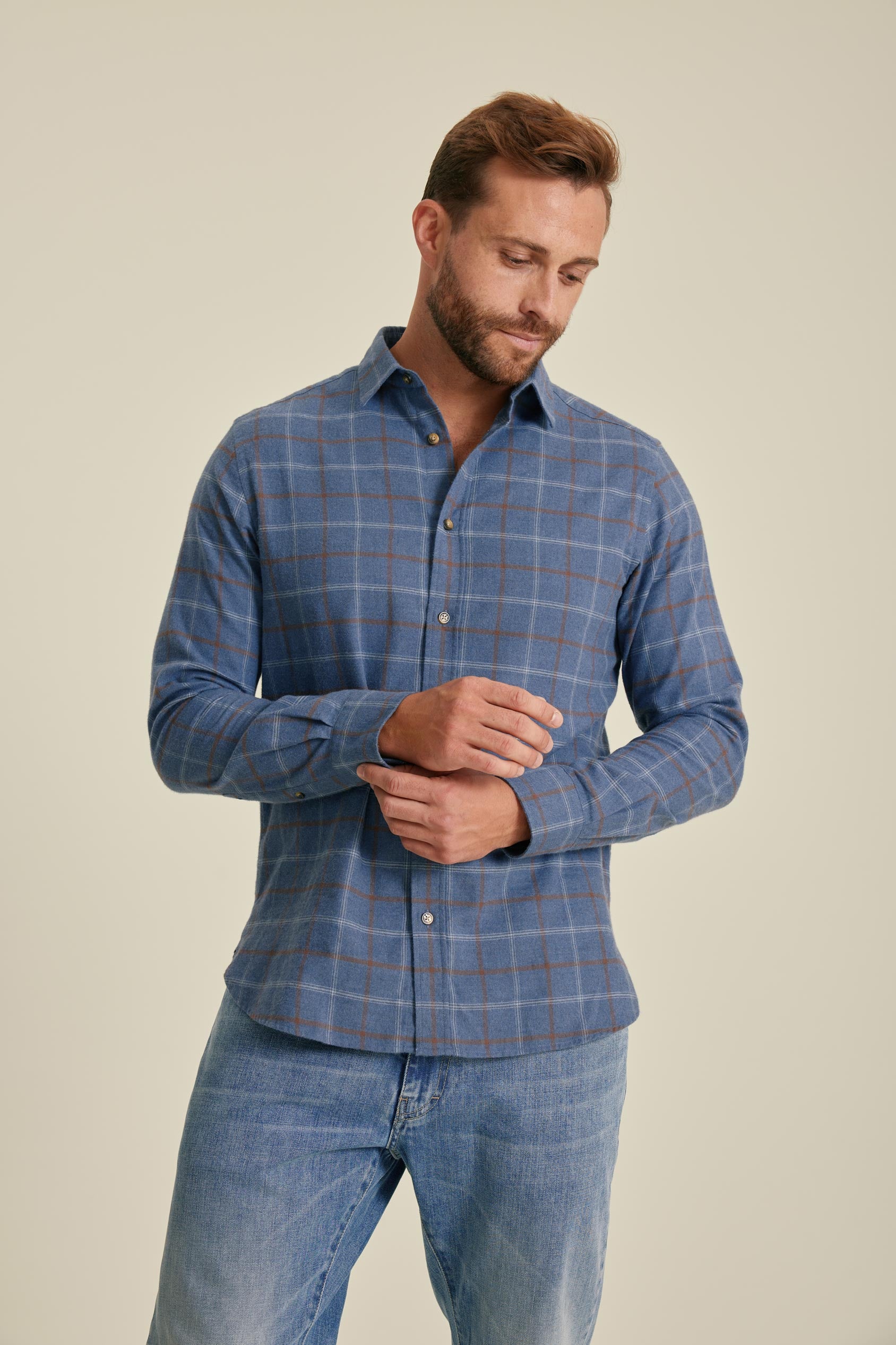 Man wearing a blue checkered shirt and jeans on a beige background