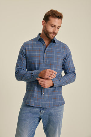 Man wearing a blue checkered shirt and jeans on a beige background