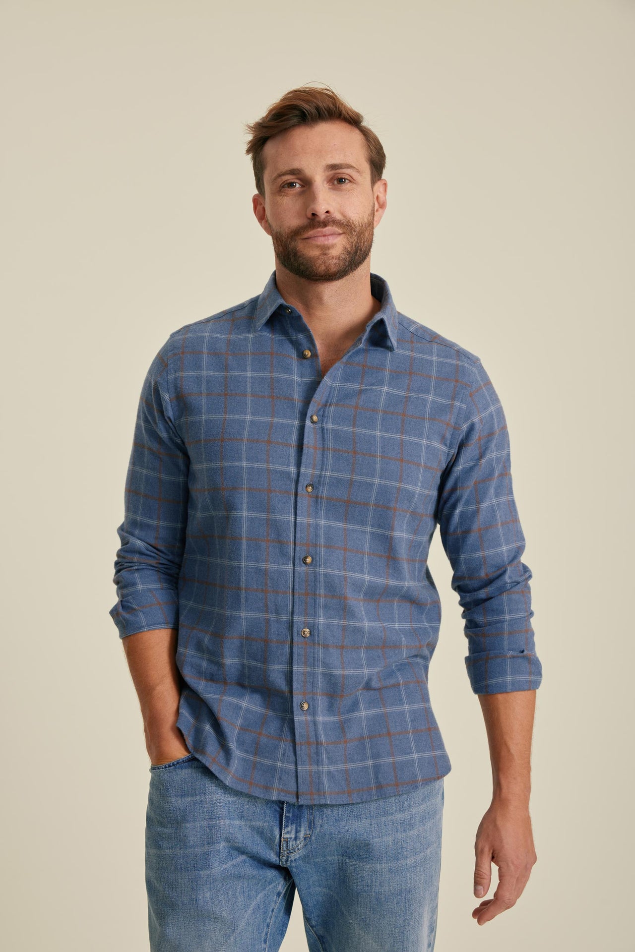 Man wearing a blue checkered shirt and jeans against a beige background