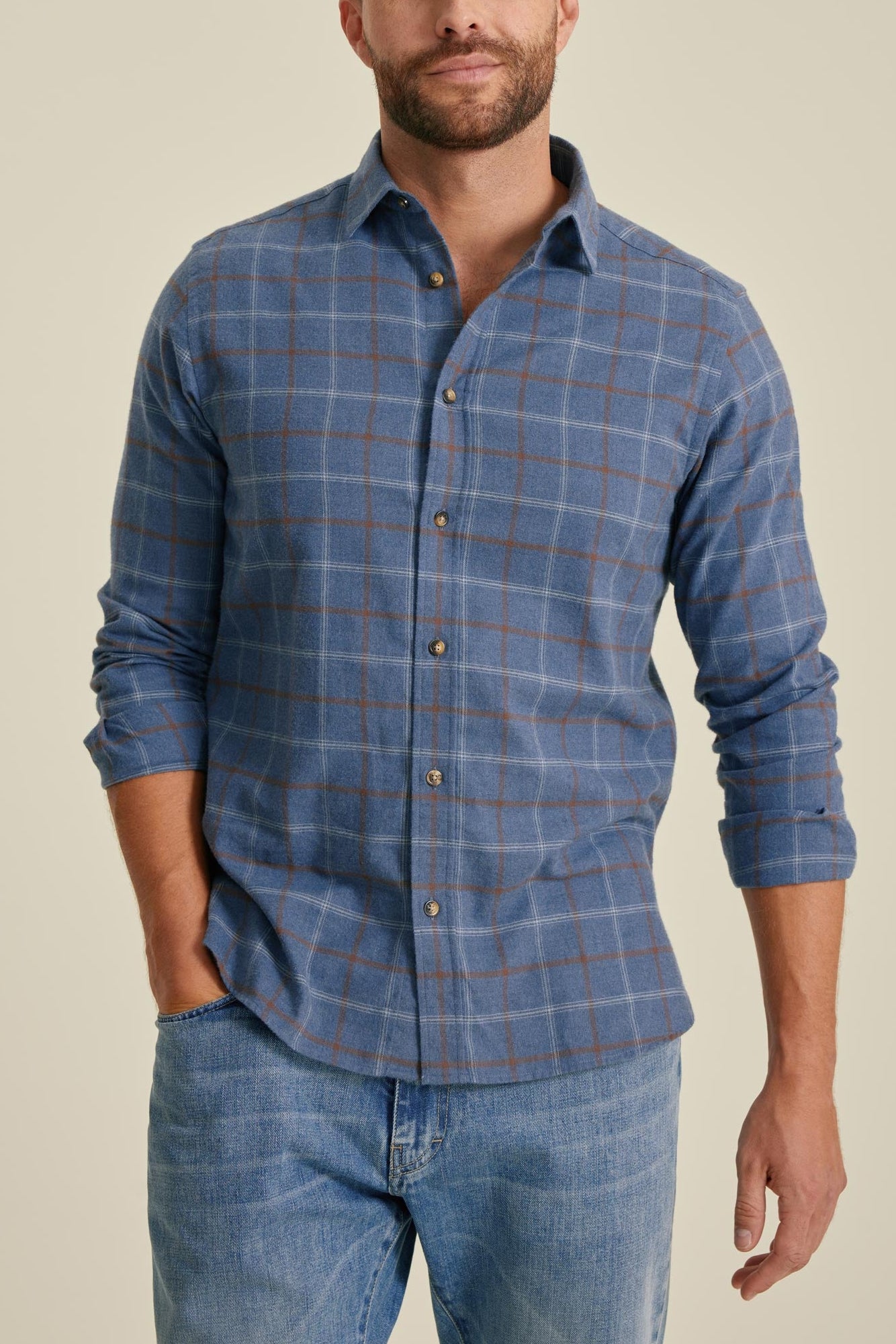 Man wearing a blue checkered shirt and jeans against a beige background
