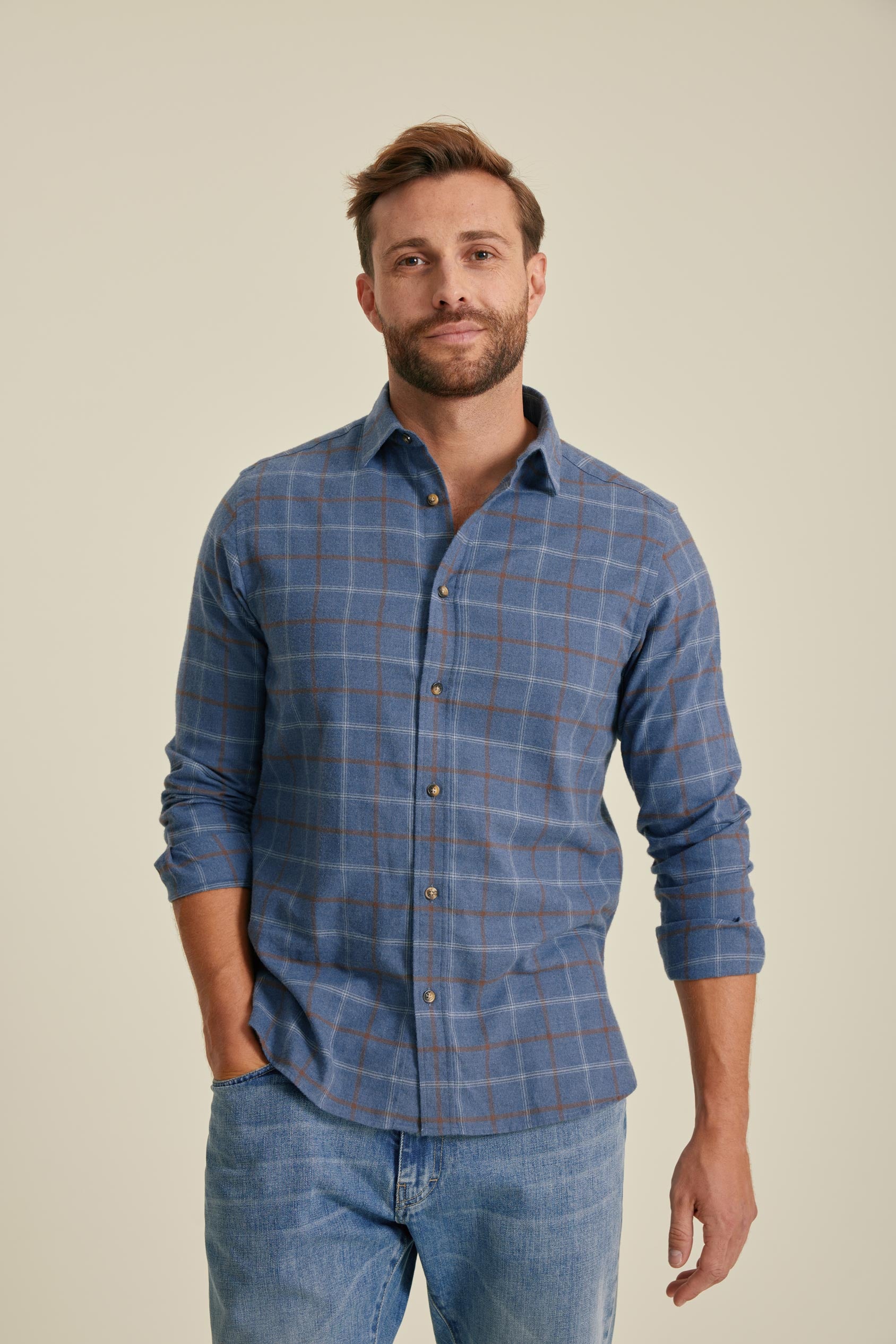 Man wearing a blue checkered shirt and jeans against a beige background