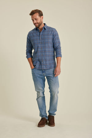 Man wearing a blue plaid shirt and jeans on a beige background