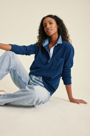 Woman wearing a blue sweater and light blue jeans sitting on a beige surface.