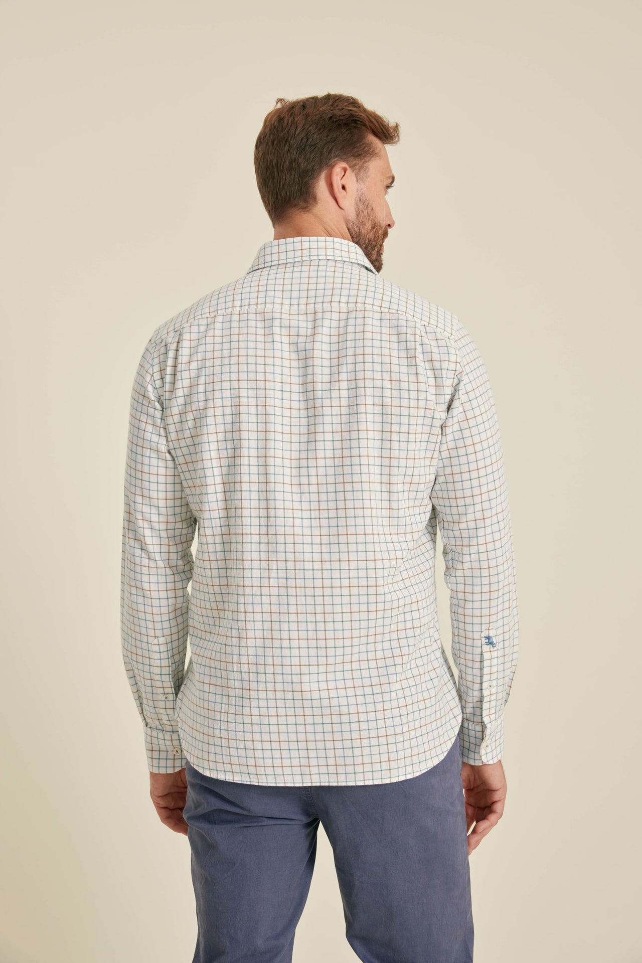 Man wearing a checkered shirt and blue pants on a beige background