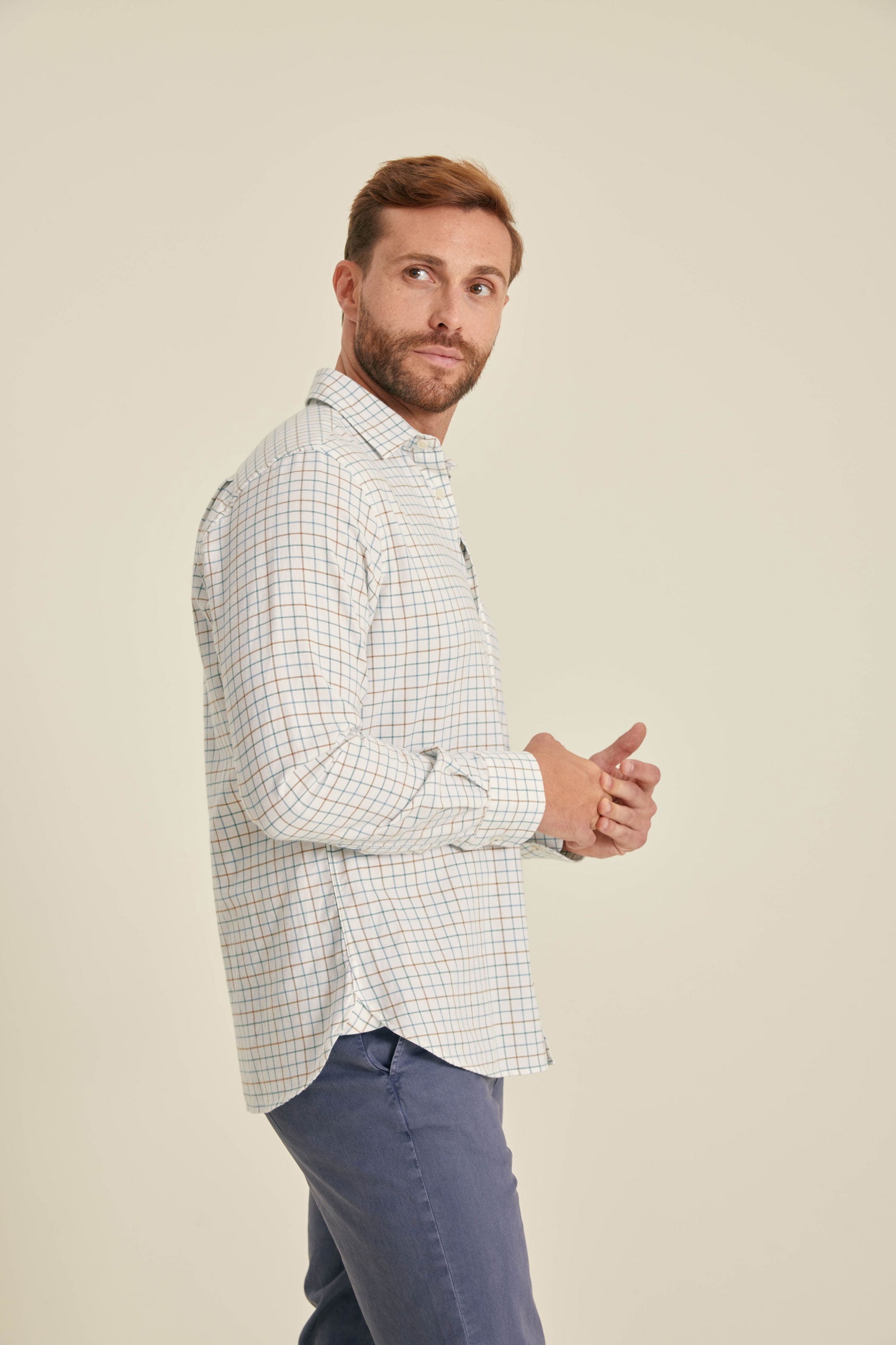 Man wearing a checkered shirt and blue pants against a beige background