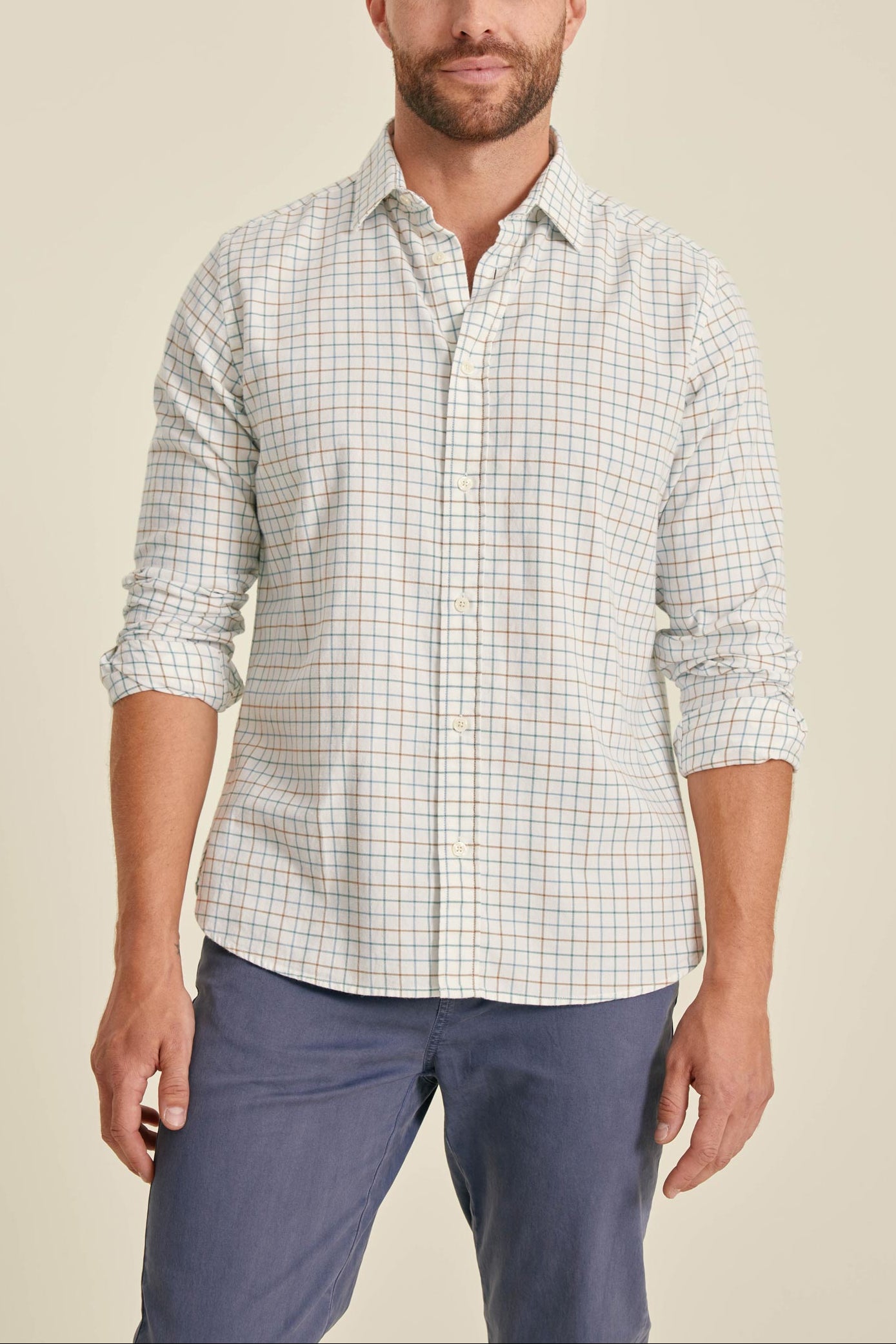 Man wearing a checkered shirt and blue pants against a beige background