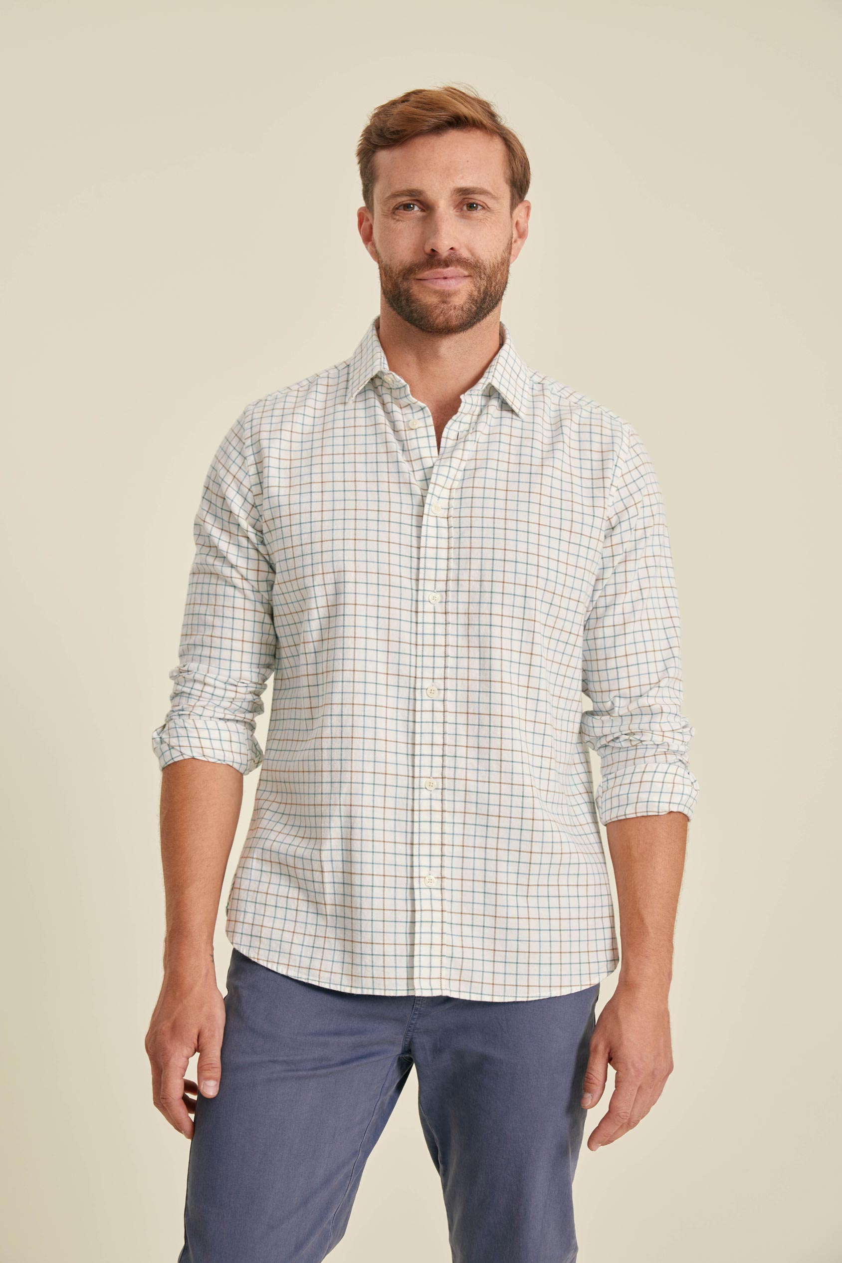 Man wearing a checkered shirt and blue pants against a beige background