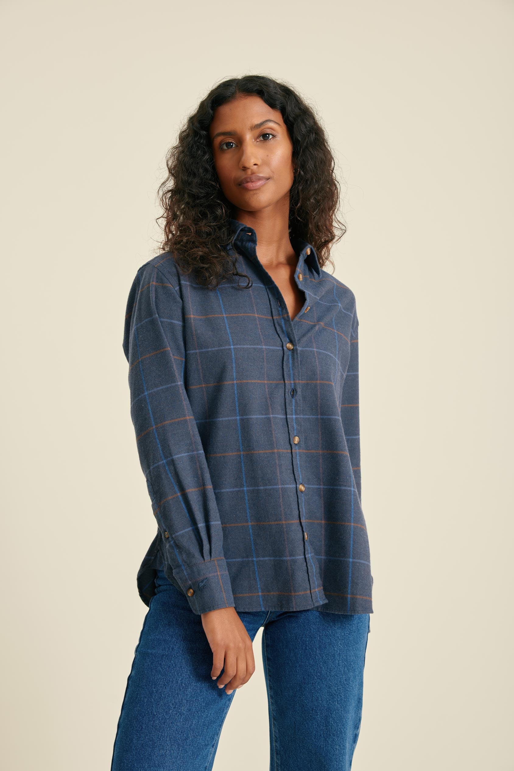 Woman wearing a blue plaid shirt and jeans on a beige background