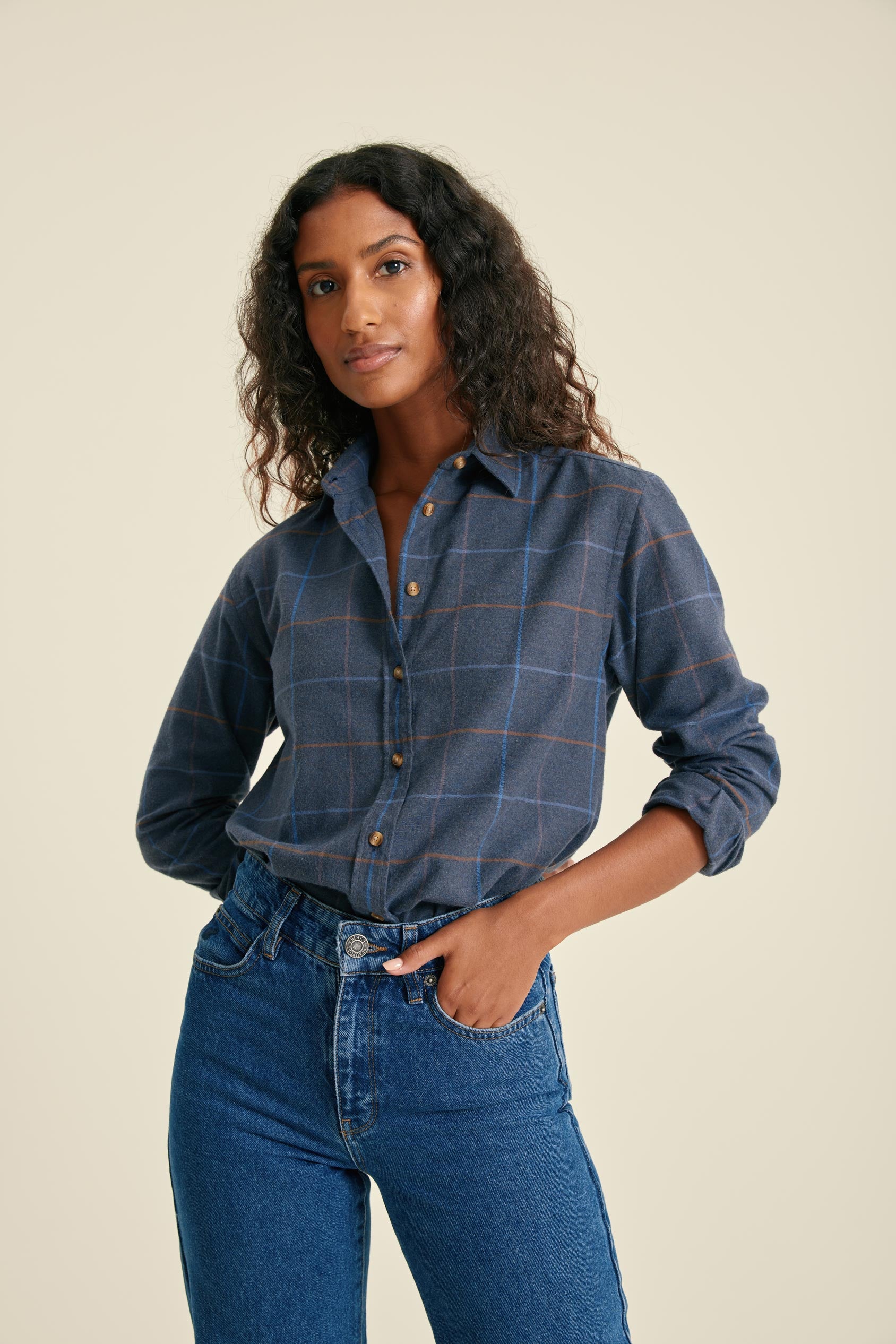Woman wearing a blue plaid shirt and jeans on a beige background