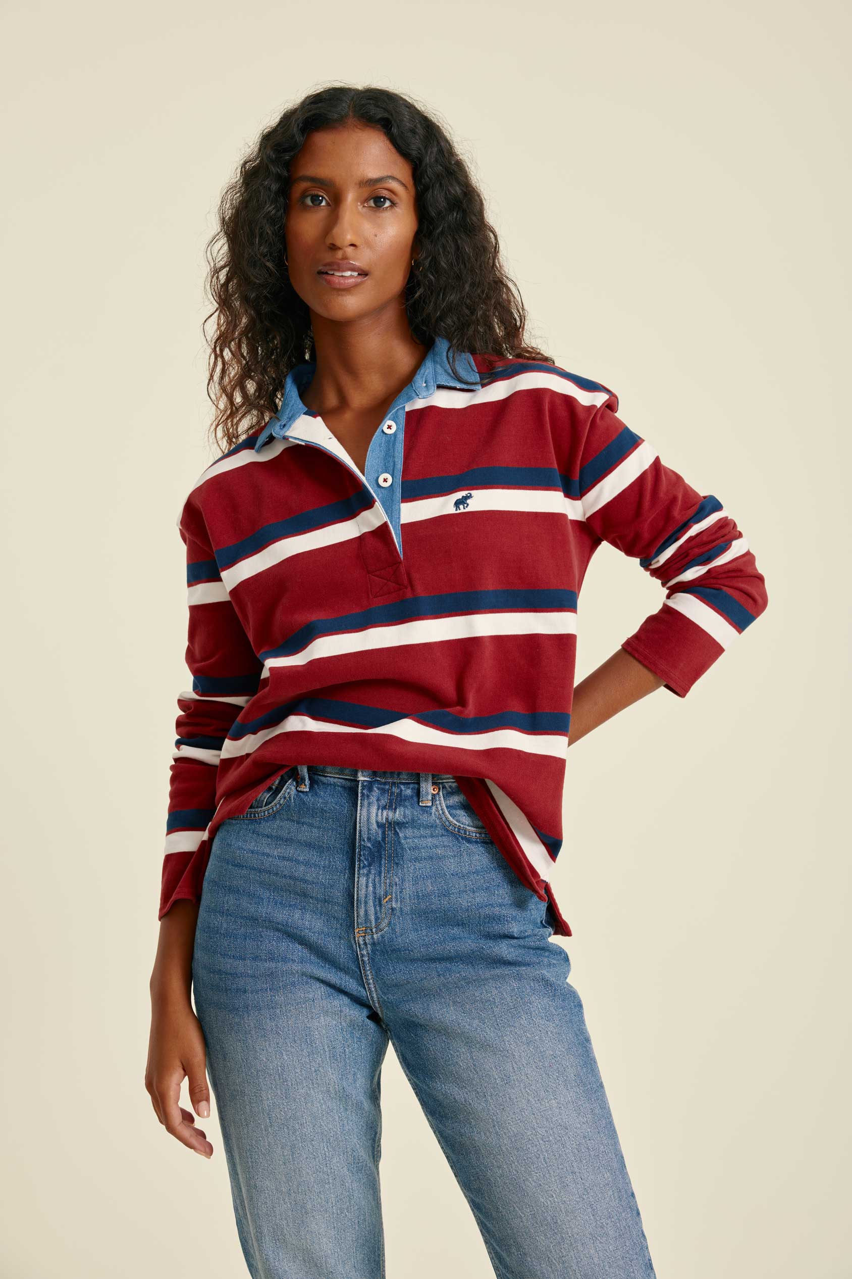 Woman wearing a red, white, and blue striped shirt with blue jeans on a beige background