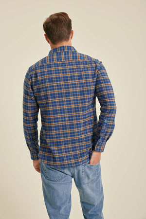 Person wearing a blue and orange plaid shirt with jeans on a beige background