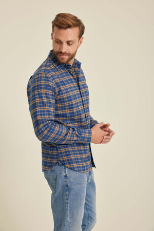 Man wearing a blue plaid shirt and jeans against a beige background