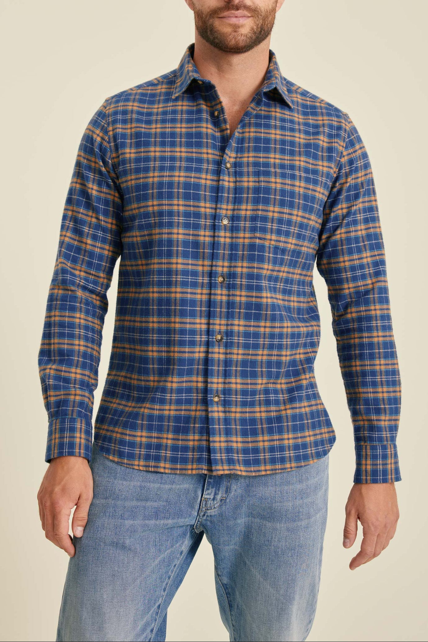 Man wearing a blue and orange plaid shirt with jeans on a beige background