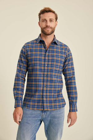 Man wearing a blue and orange plaid shirt with jeans on a beige background