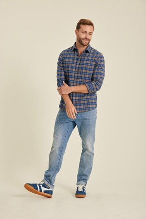 Man wearing a blue plaid shirt and jeans standing against a beige background