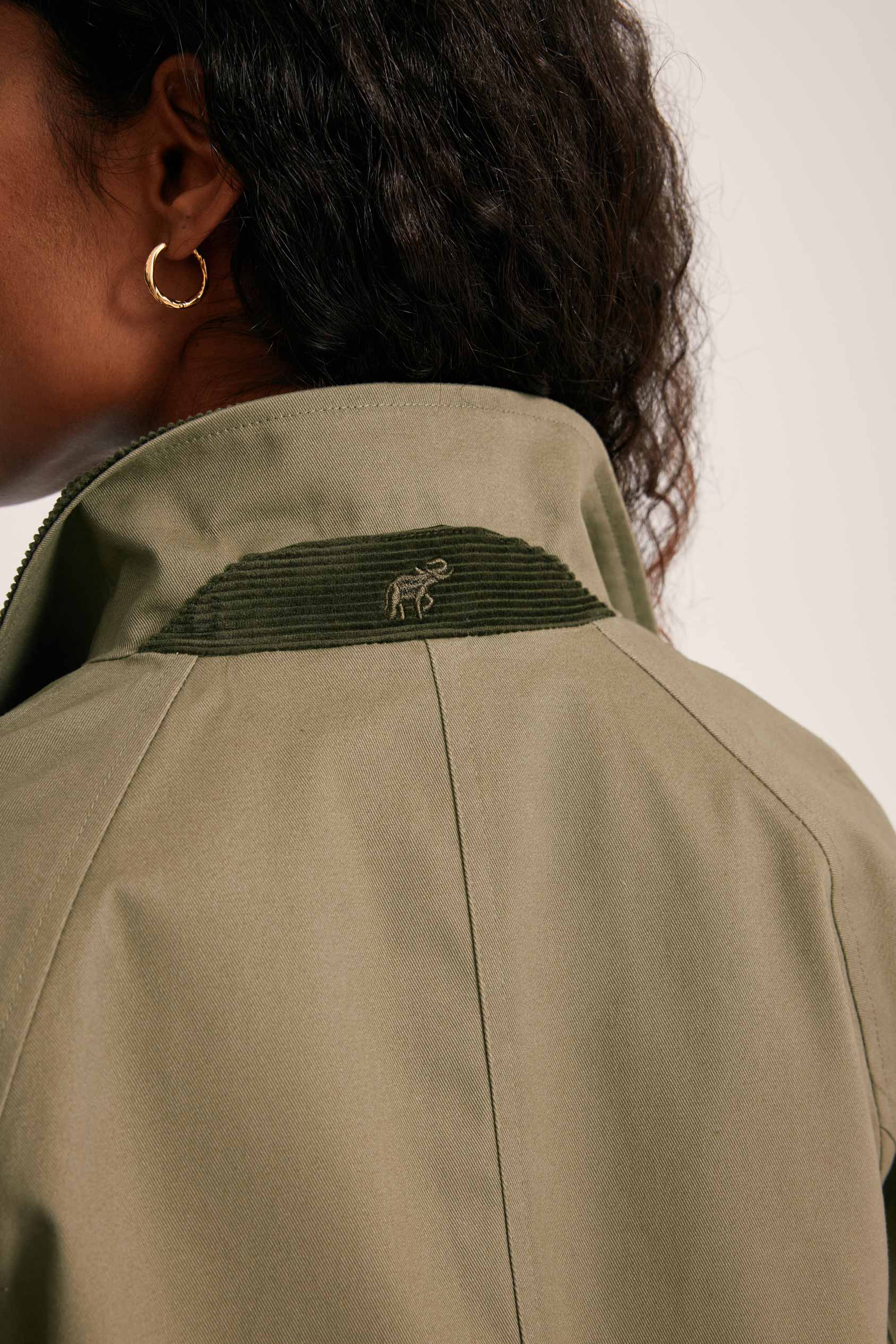 Close-up of a person wearing a green jacket with a logo on the collar against a white background