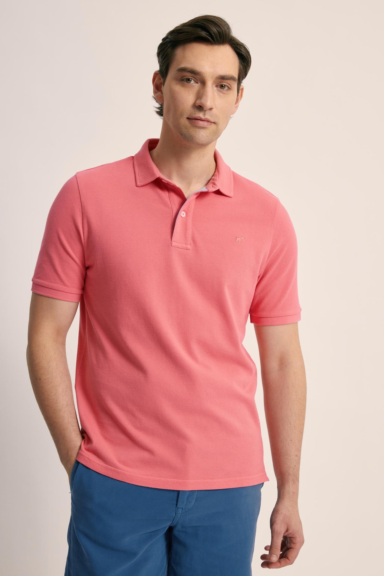 Man wearing a pink polo shirt and blue pants on a beige background