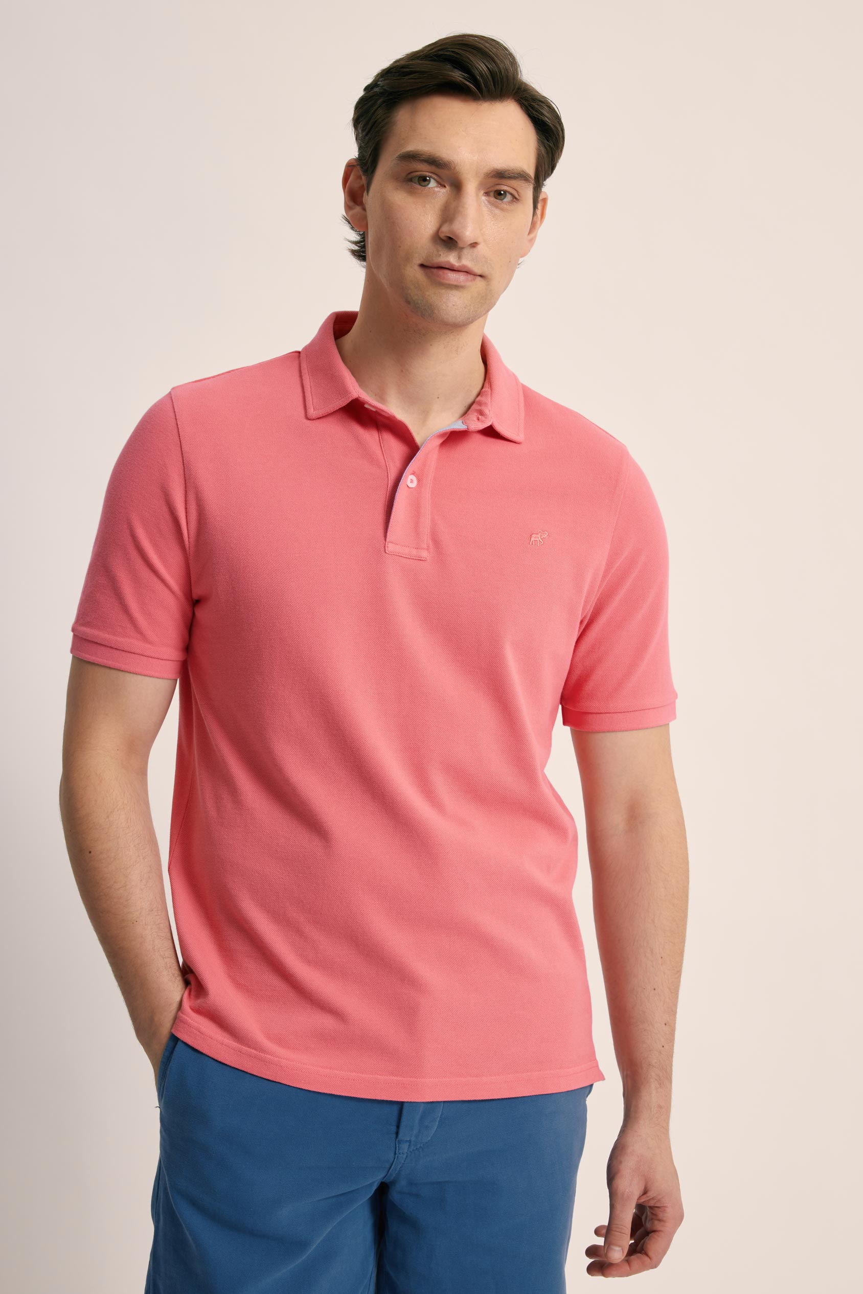 Man wearing a pink polo shirt and blue pants on a beige background