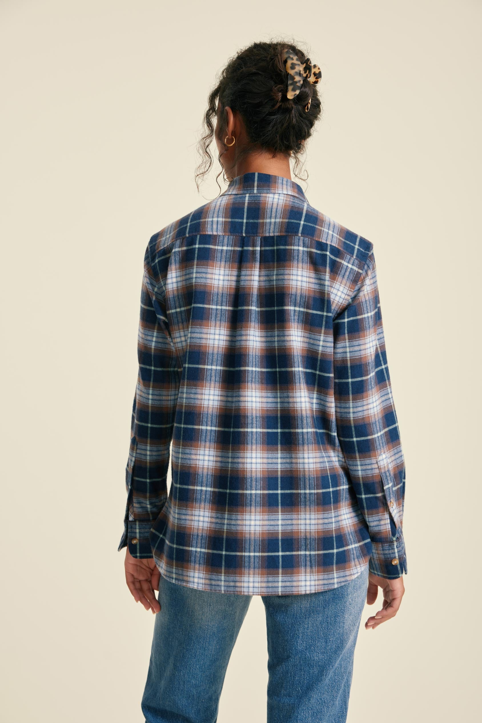 Person wearing a blue and brown plaid shirt on a beige background