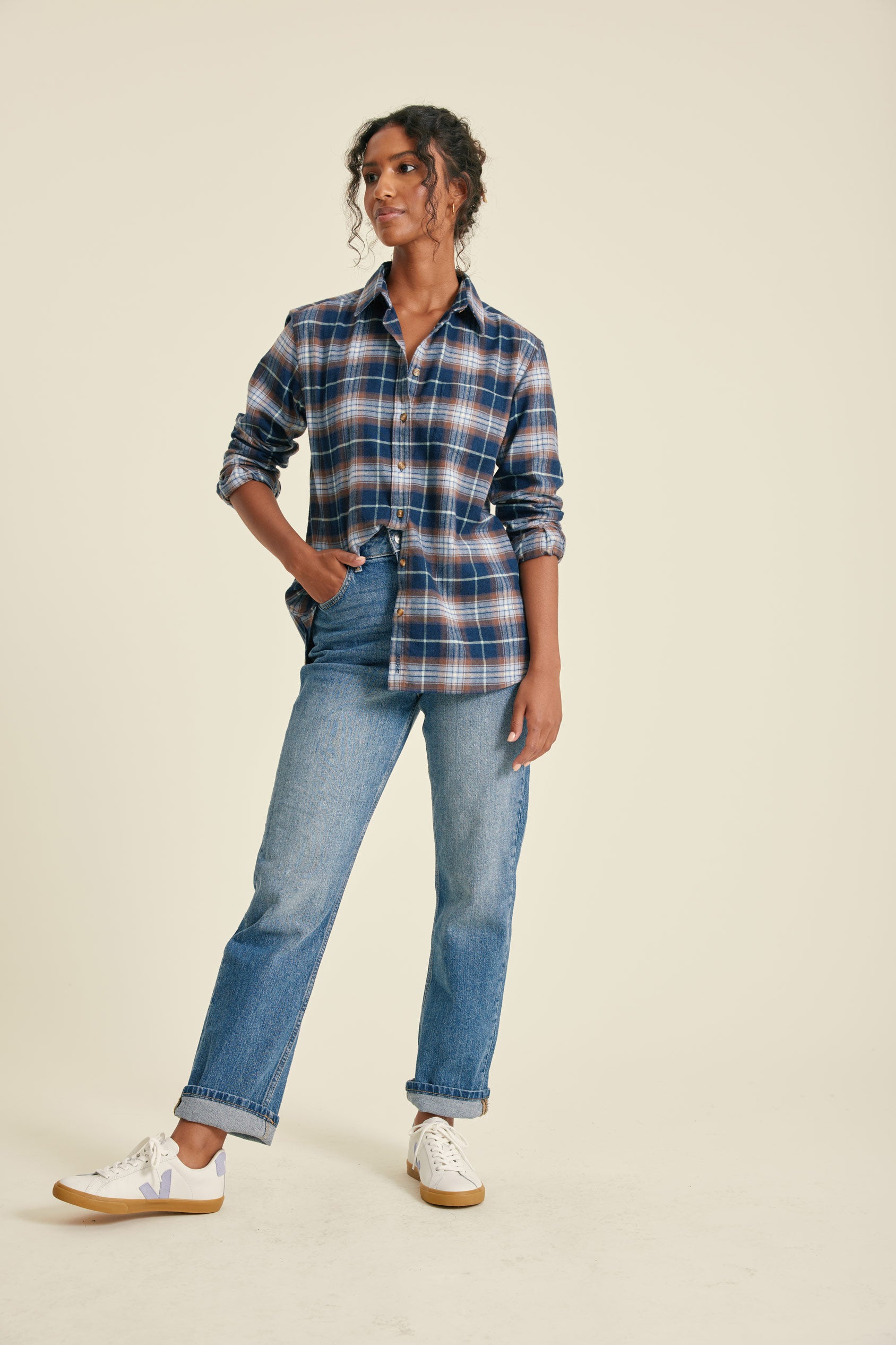 Woman wearing a plaid shirt and jeans on a beige background