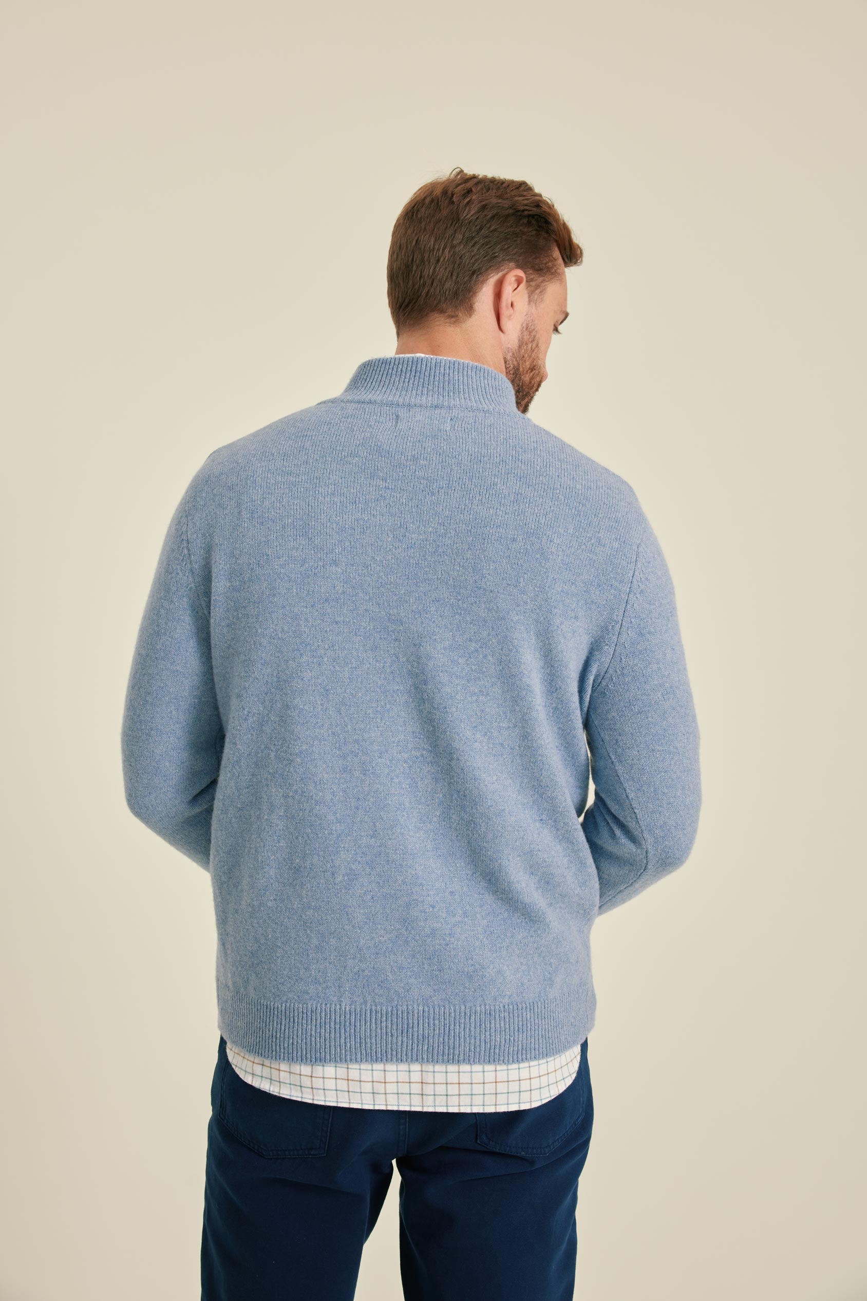 Man wearing a blue sweater and navy pants on a beige background