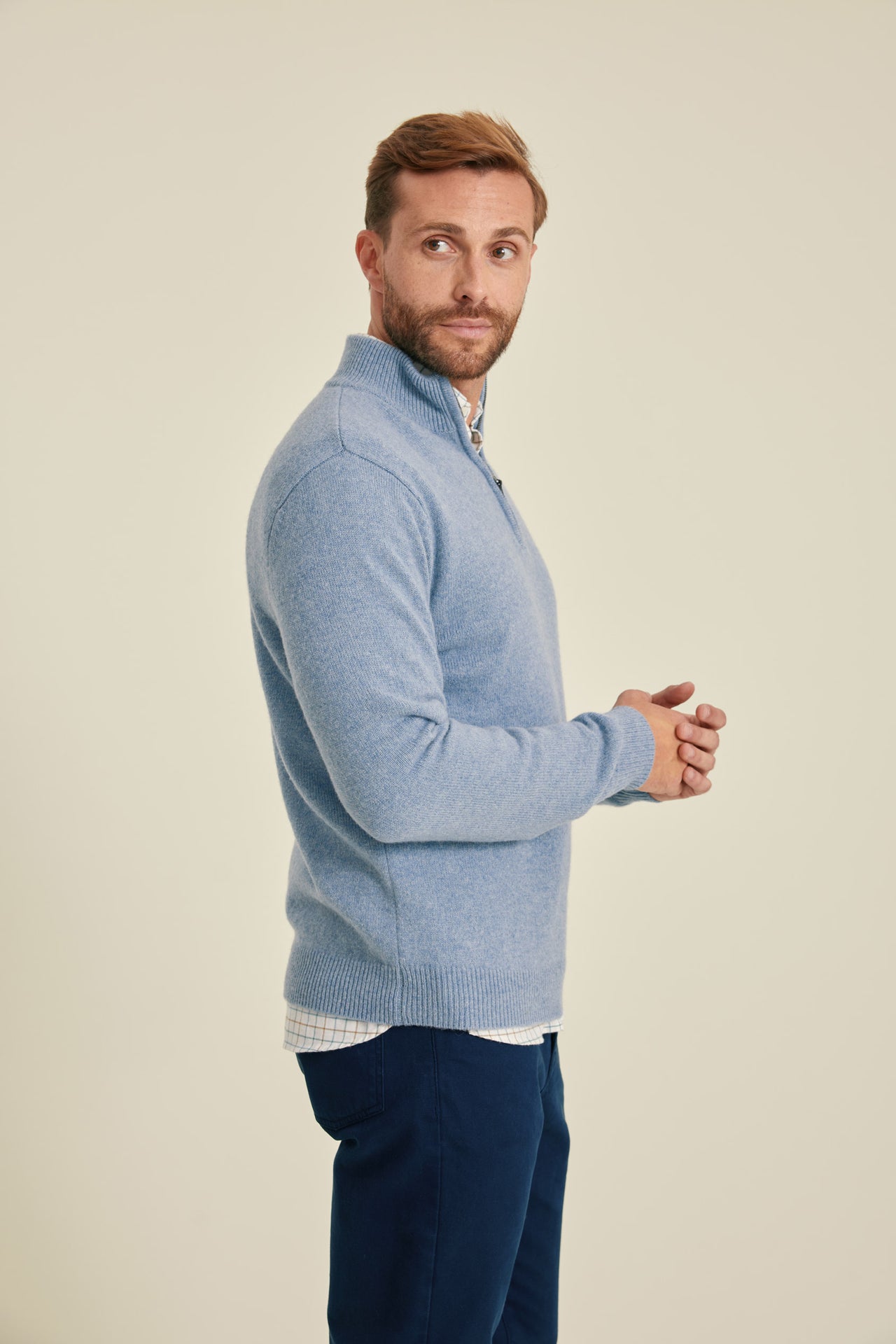 Man wearing a light blue sweater and dark blue pants on a beige background