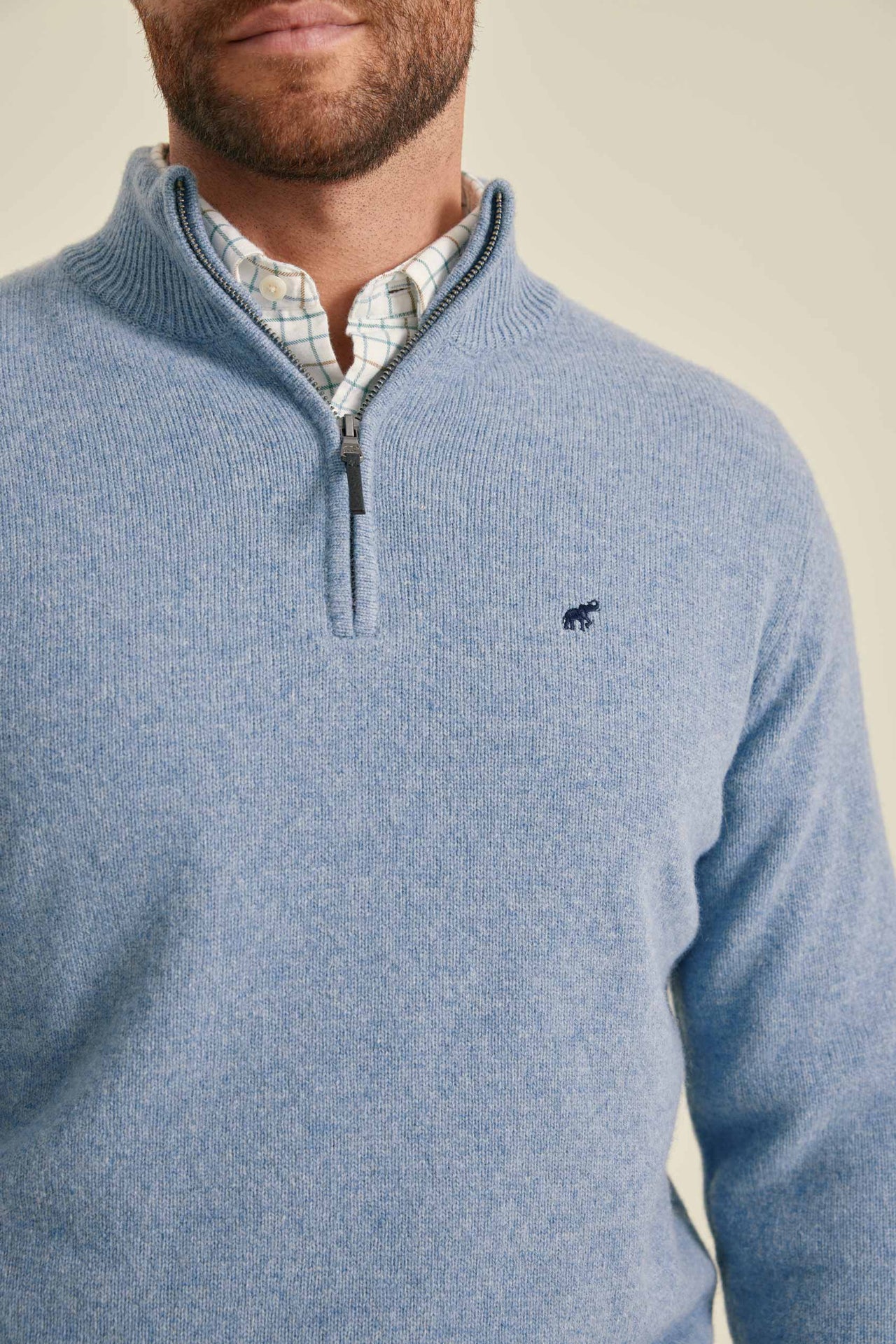 Man wearing a blue quarter-zip sweater with a brand logo on a beige background