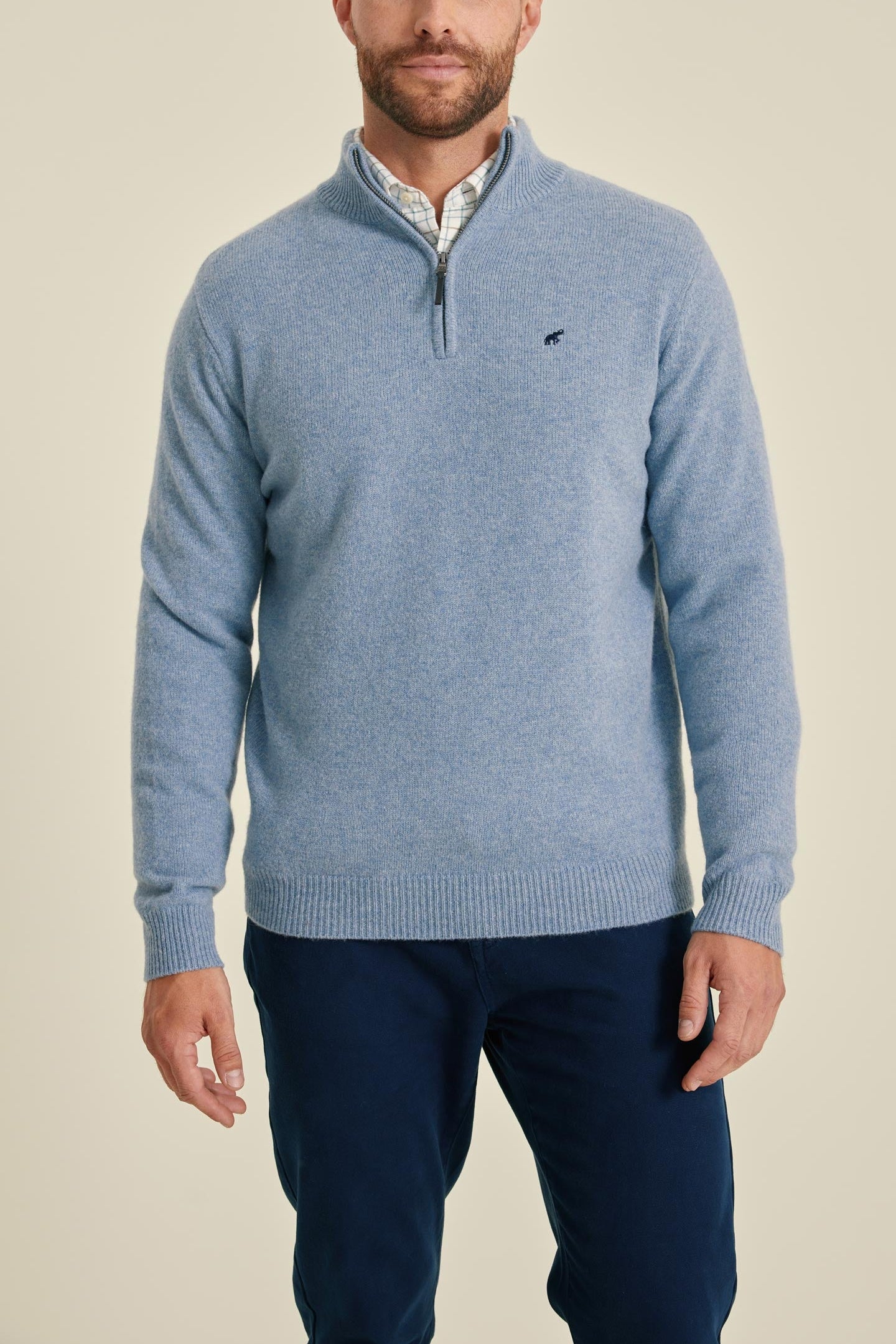 Man wearing a blue sweater with a small logo on a beige background