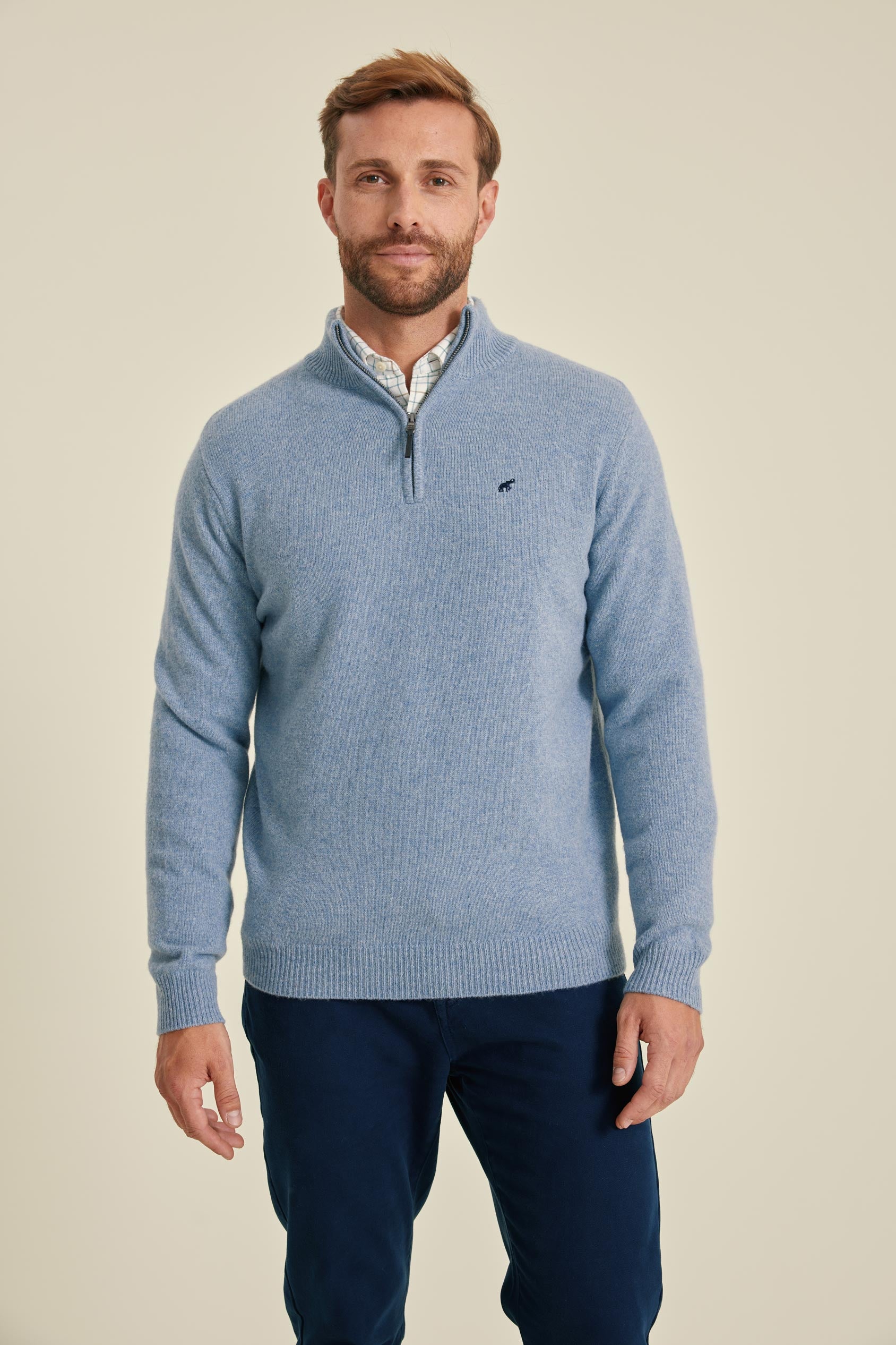Man wearing a blue sweater with a small logo on a beige background