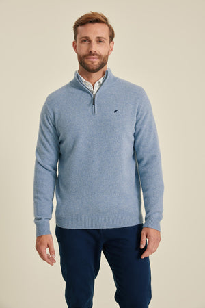 Man wearing a blue sweater with a small logo on a beige background