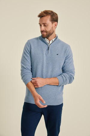 Man wearing a blue sweater and dark pants on a beige background