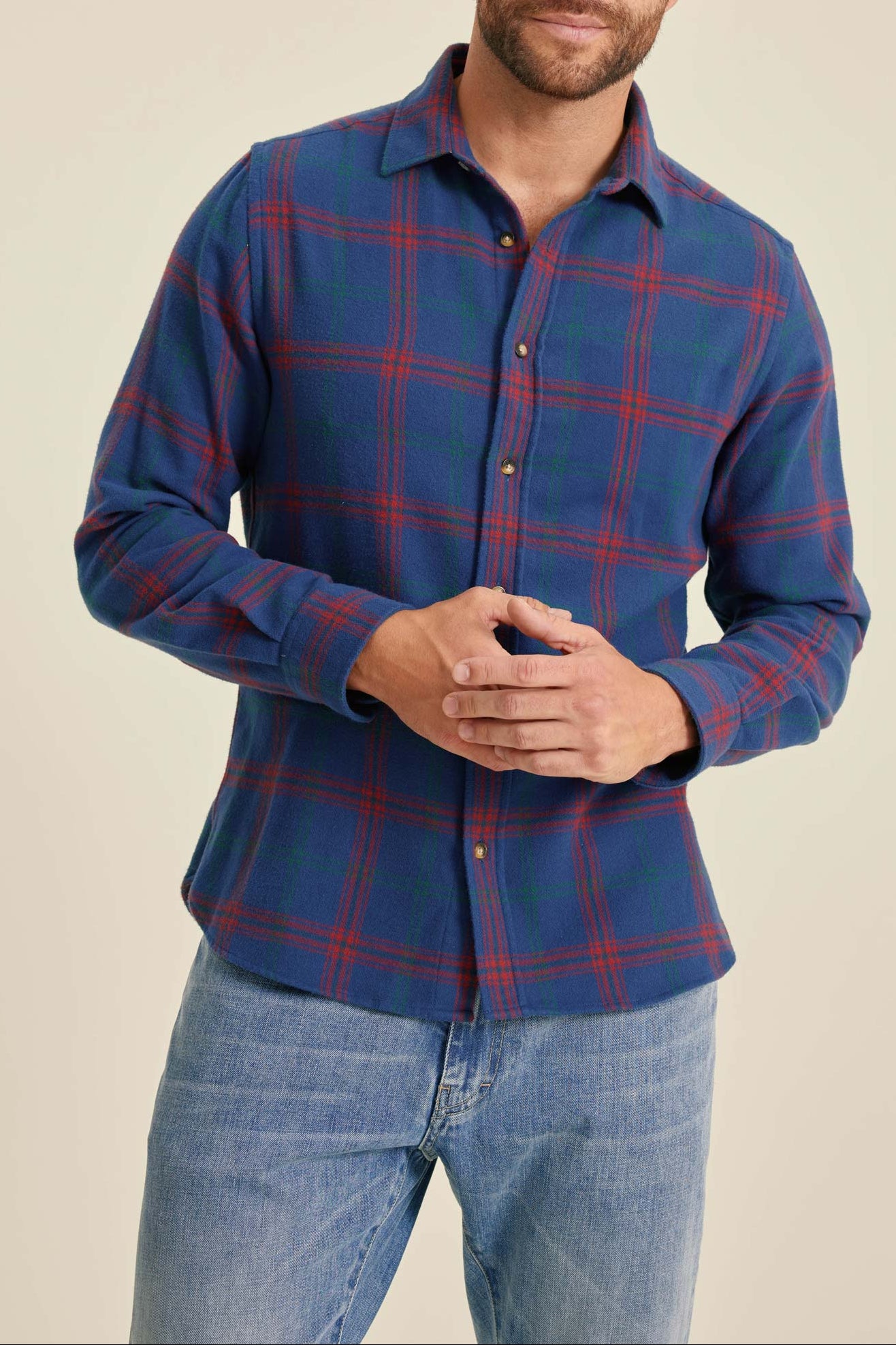 Man wearing a blue plaid shirt and jeans on a beige background