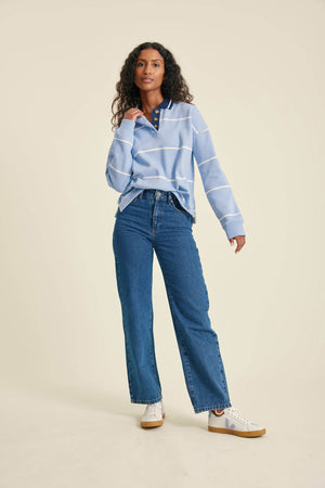 Woman wearing a light blue striped sweater and blue jeans on a beige background
