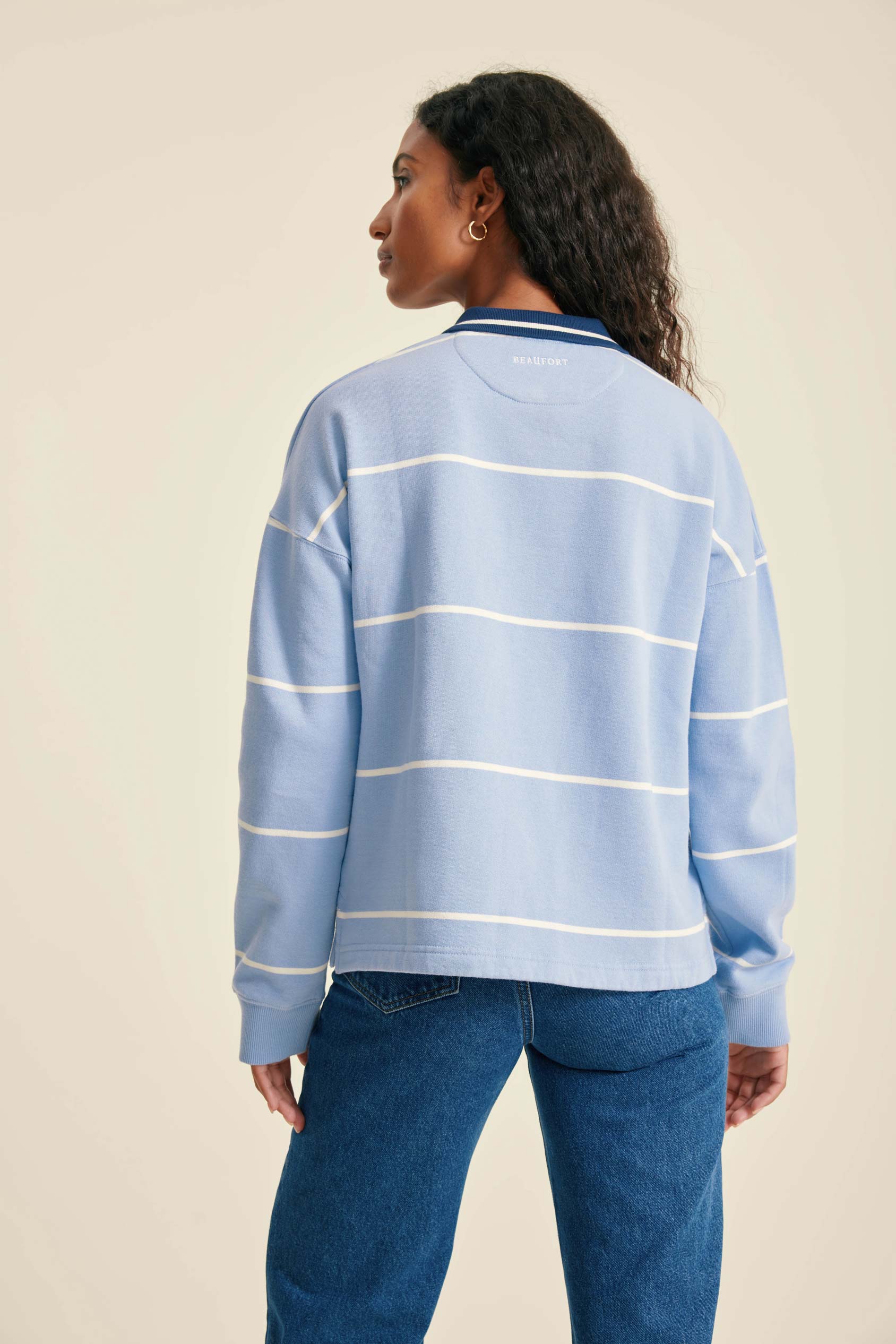 Person wearing a light blue striped sweater and blue jeans on a beige background