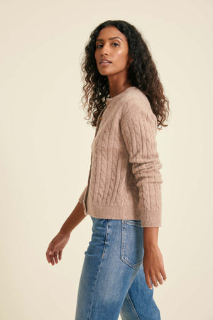 Woman wearing a beige cable knit sweater and blue jeans on a beige background