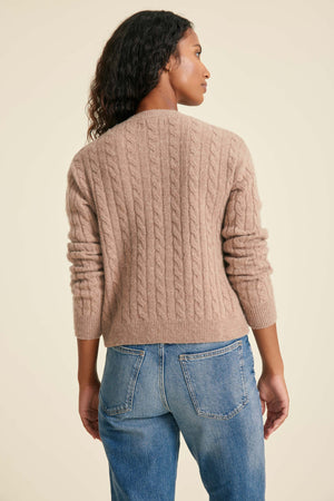 Woman wearing a beige cable knit sweater and blue jeans on a beige background