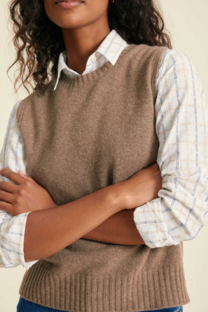 Person wearing a brown sweater vest over a plaid shirt with arms crossed.