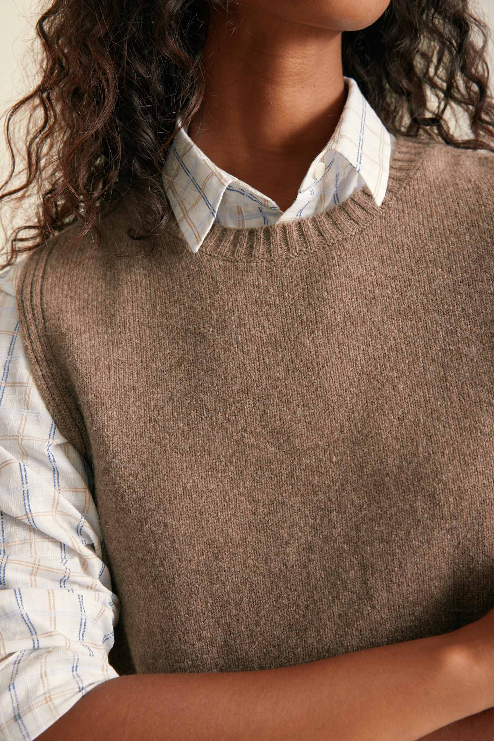 Person wearing a brown knitted vest over a plaid shirt